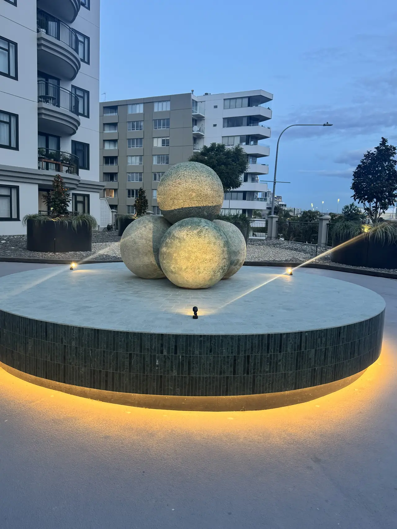 Lit circular mosaic fountain plinth at dusk